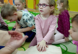 Dziewczynka uczy się wykonywać masaż serca na fantomie