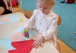 Ala siedzi przy stoliku. Smaruje klejem czerwoną czapkę Mikołaja.