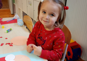 Nela w czerwonej bluzce siedzi przy stoliku. Przed nią leży rozpoczęta praca, którą starannie ozdabia, rozwijając swoją kreatywność i zdolności manualne