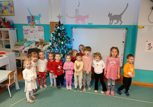 Wszystkie dzieci stoją razem wokół ubranęj choinki, podziwiając wspólnie efekty swojej pracy i ciesząc się świąteczną atmosferą