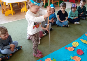 Dziewczynka łowi na wędkę papierową sylwetę ryby