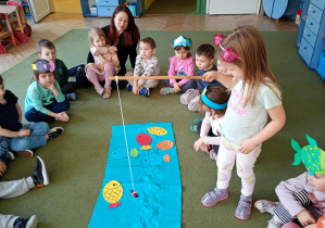 Dziewczynka łowi na wędkę papierową sylwetę ryby