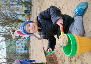Chłopiec napełnia wiaderko piaskiem