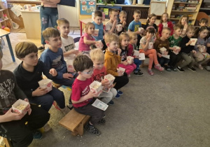 Dzieci siedzą na krzesełkach i jedzą popcorn